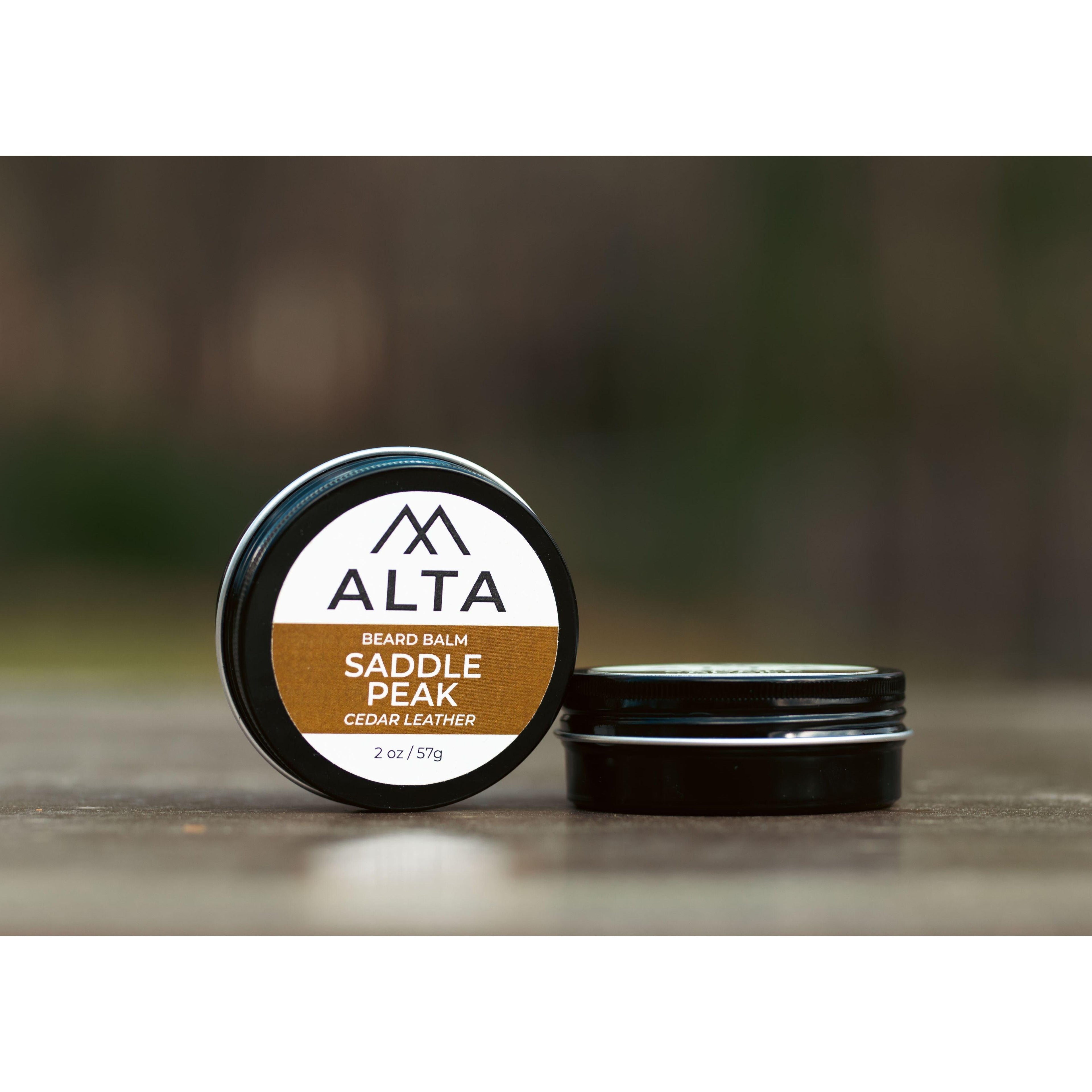 Alta Body Saddle Peak Premium Beard Balm in a 2oz black tin resting on a wooden surface. Natural cedar and leather scent.
